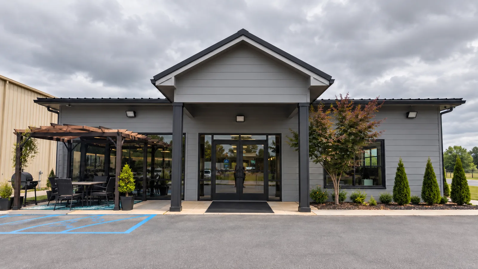 The S.N.A.P. Academy building in Huntsville, Alabama: a single-storey grey building with a covered entrance, a pergola and outdoor seating to one side, and young trees along the front.