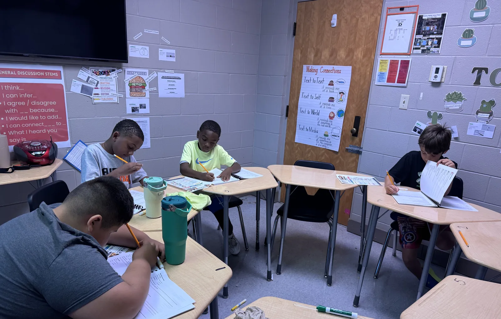 Students writing at desks spread across the room, under the wall chart of discussion stems — I think, I can infer, I agree, I disagree.