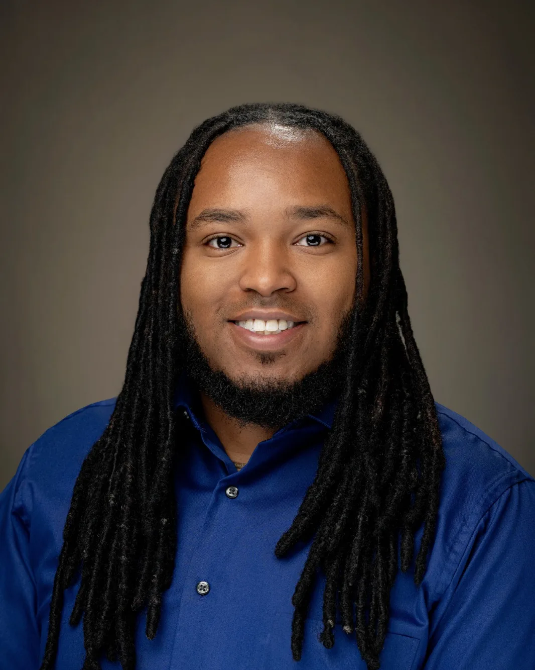 Christopher Jeremiah Holden, smiling, in a blue shirt against a dark background.