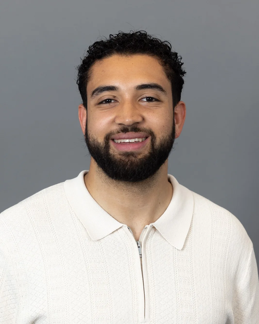 Evan Tenorio, smiling, in a cream polo shirt against a grey background.